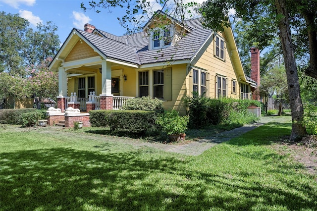 view of front of home with a porch, a chimney, and a front yard