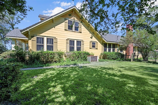 rear view of house featuring a lawn, a chimney, and fence