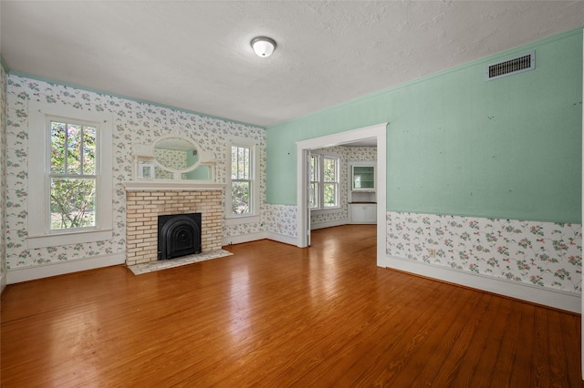unfurnished living room with visible vents, a textured ceiling, wood finished floors, wallpapered walls, and baseboards