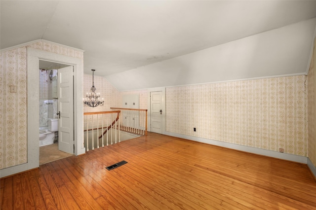 additional living space with hardwood / wood-style floors, visible vents, wallpapered walls, vaulted ceiling, and a chandelier