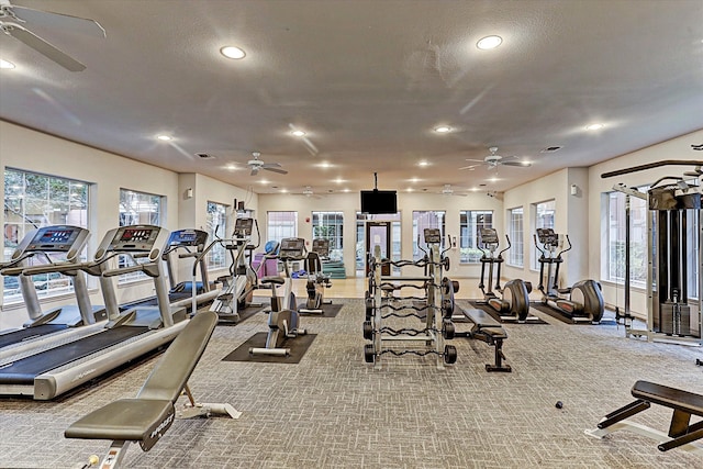 workout area featuring ceiling fan, light colored carpet, and a textured ceiling