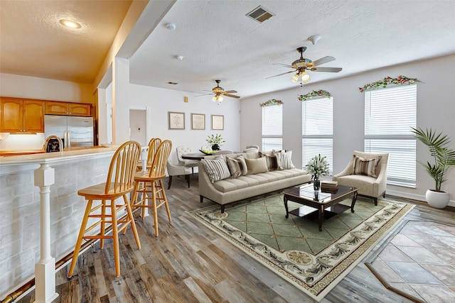 living room with ceiling fan, light wood-type flooring, and a textured ceiling