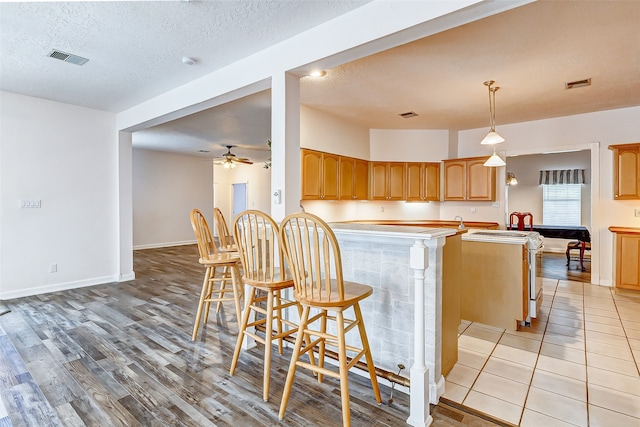 kitchen featuring light hardwood / wood-style floors, pendant lighting, a kitchen breakfast bar, kitchen peninsula, and a textured ceiling