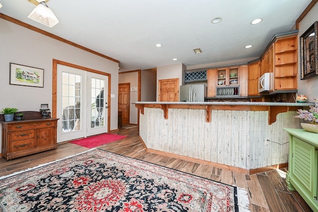 kitchen featuring crown molding, stainless steel fridge, dark hardwood / wood-style flooring, kitchen peninsula, and a breakfast bar area