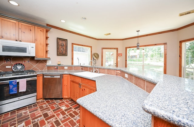 kitchen with appliances with stainless steel finishes, light stone counters, sink, pendant lighting, and tasteful backsplash