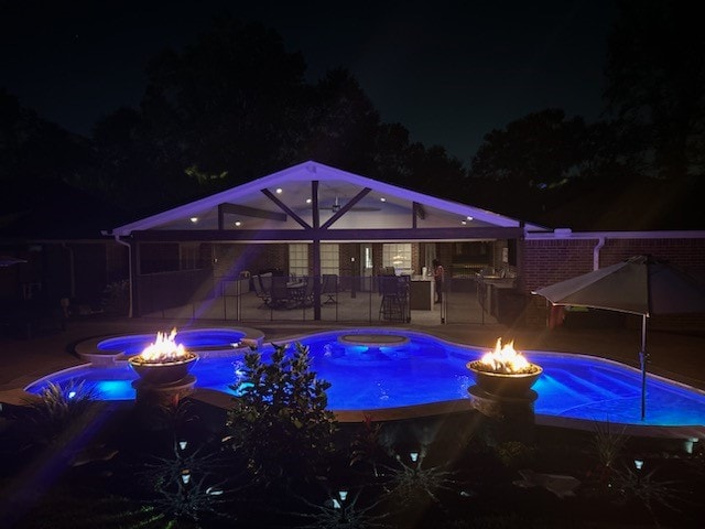 pool at twilight with an in ground hot tub, a patio area, and an outdoor fire pit