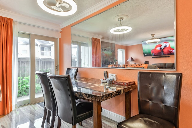 dining space featuring ornamental molding, light wood-type flooring, a textured ceiling, and a wealth of natural light