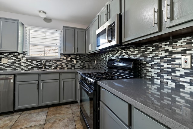 kitchen with gray cabinetry, backsplash, dark tile patterned floors, appliances with stainless steel finishes, and sink