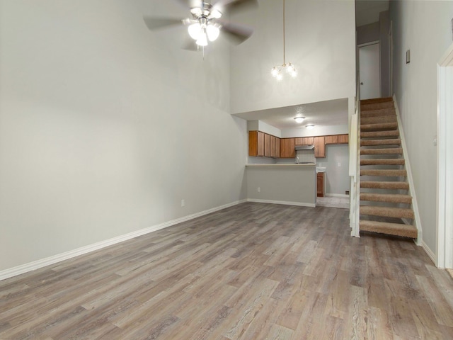 unfurnished living room with a high ceiling, ceiling fan with notable chandelier, and light hardwood / wood-style floors