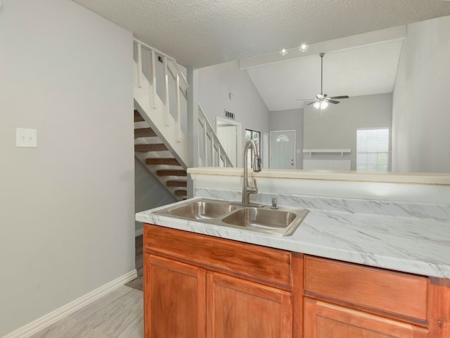 kitchen with a textured ceiling, sink, ceiling fan, vaulted ceiling, and light hardwood / wood-style floors