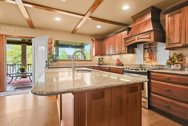 kitchen featuring custom exhaust hood, stainless steel range oven, an island with sink, sink, and light hardwood / wood-style floors