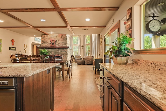 kitchen featuring coffered ceiling, light stone countertops, a stone fireplace, beam ceiling, and light hardwood / wood-style floors