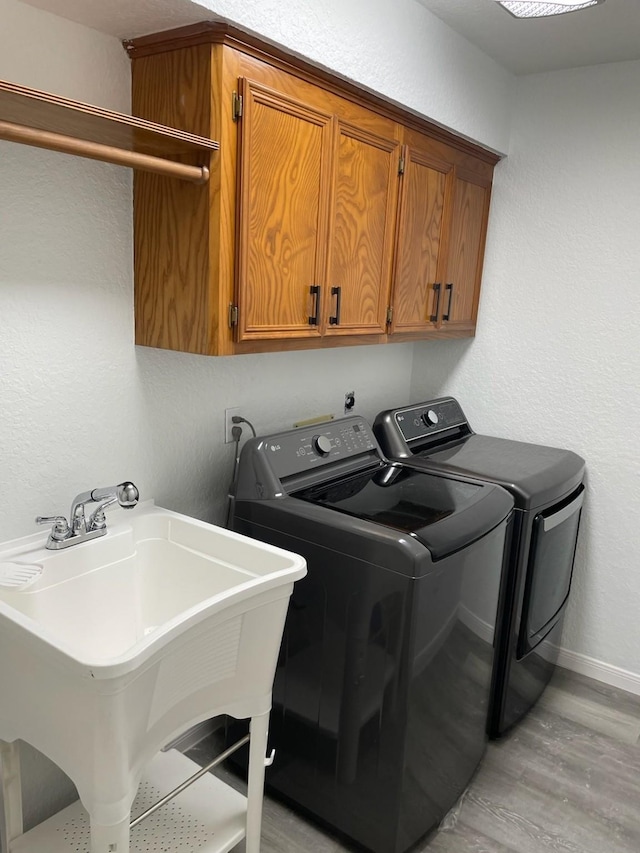 washroom with light wood-type flooring, sink, separate washer and dryer, and cabinets