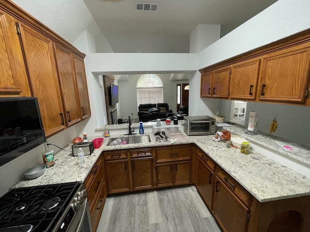 kitchen featuring stainless steel gas stove, sink, light hardwood / wood-style flooring, and light stone countertops