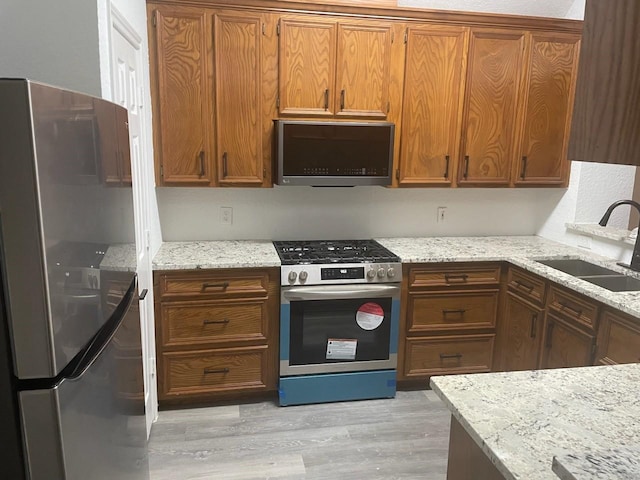 kitchen with light wood-type flooring, light stone countertops, appliances with stainless steel finishes, and sink