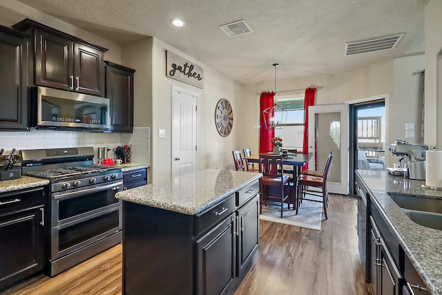 kitchen with hanging light fixtures, light hardwood / wood-style floors, a textured ceiling, a kitchen island, and appliances with stainless steel finishes