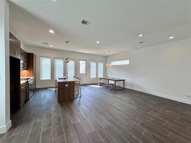 interior space featuring an island with sink, stainless steel appliances, dark hardwood / wood-style flooring, and a breakfast bar area