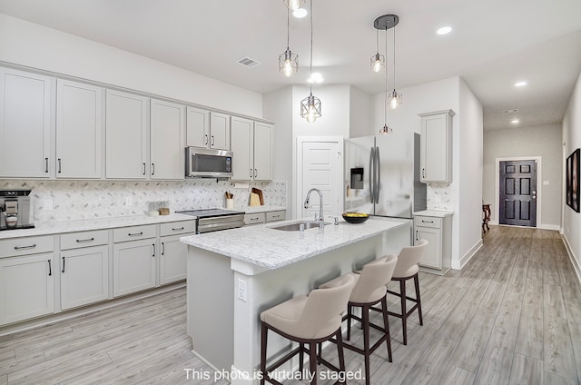 kitchen with sink, an island with sink, appliances with stainless steel finishes, light hardwood / wood-style floors, and a breakfast bar area