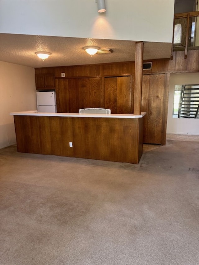 kitchen featuring white refrigerator, a textured ceiling, kitchen peninsula, and wood walls