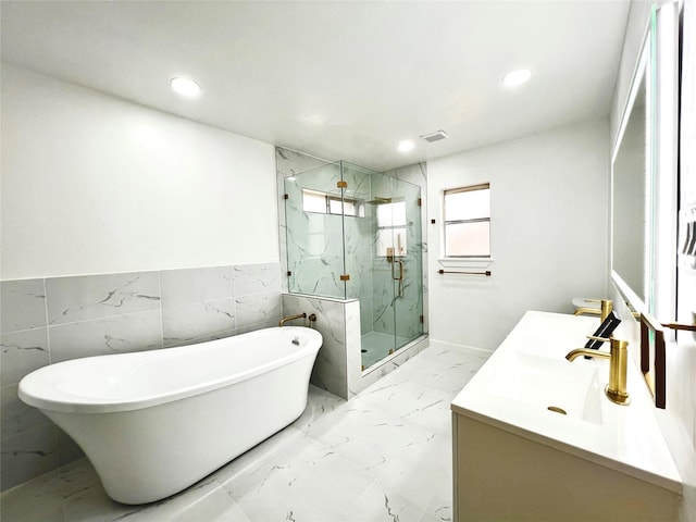 bathroom featuring a freestanding tub, marble finish floor, recessed lighting, a marble finish shower, and vanity