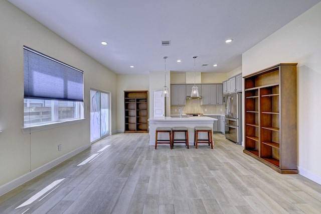 kitchen with stainless steel fridge with ice dispenser, decorative light fixtures, gray cabinets, decorative backsplash, and a center island with sink