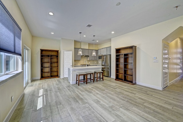 kitchen with stainless steel appliances, wall chimney range hood, decorative light fixtures, gray cabinets, and a kitchen island with sink