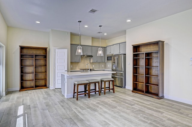 kitchen with pendant lighting, a kitchen island with sink, sink, appliances with stainless steel finishes, and tasteful backsplash