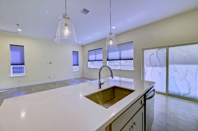 kitchen with an island with sink, stainless steel dishwasher, hanging light fixtures, and sink