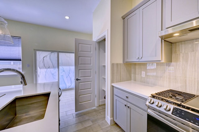 kitchen featuring sink, ventilation hood, gray cabinets, and stainless steel range with gas stovetop