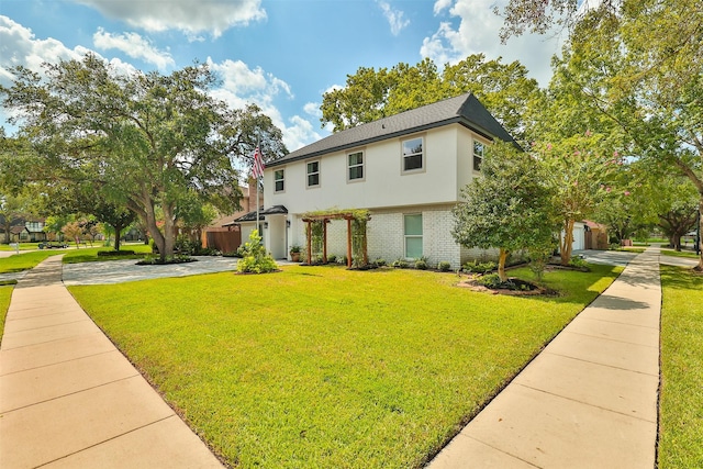 colonial inspired home featuring stucco siding, driveway, brick siding, and a front lawn