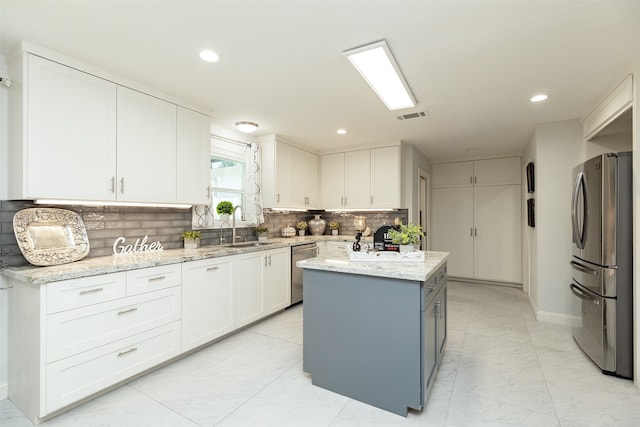 kitchen with a kitchen island, stainless steel appliances, sink, white cabinetry, and light stone counters