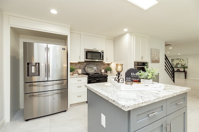 kitchen with light stone countertops, a center island, stainless steel appliances, gray cabinets, and white cabinetry