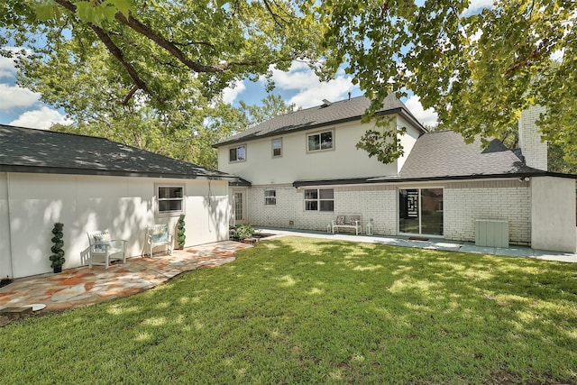 back of house featuring a yard, a patio area, brick siding, and a chimney