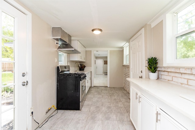 kitchen with stainless steel gas range, a sink, light countertops, white cabinets, and wall chimney exhaust hood