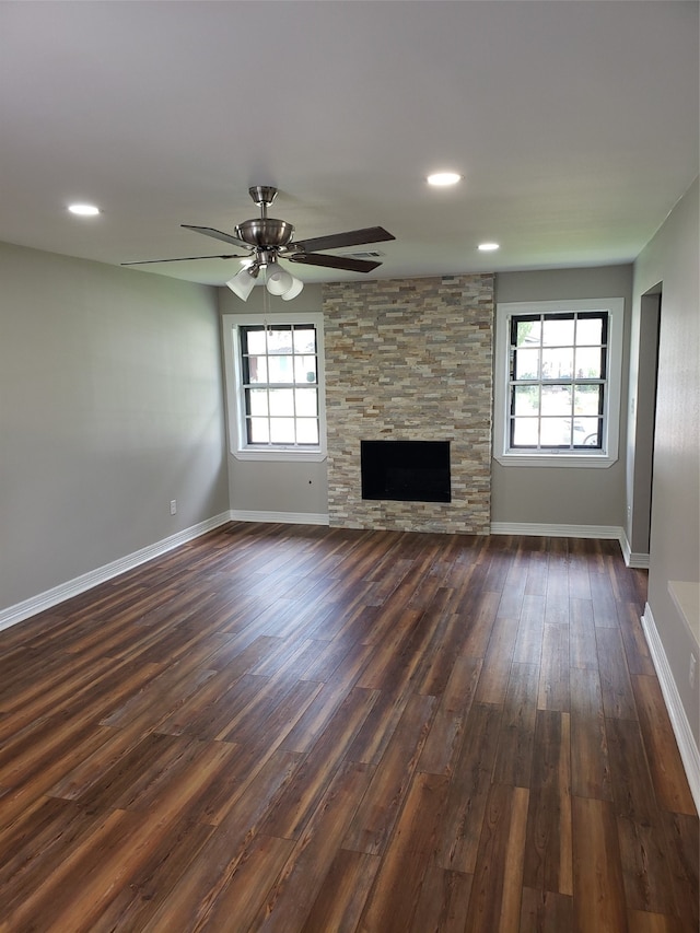 unfurnished living room with a stone fireplace, dark wood-type flooring, a healthy amount of sunlight, and ceiling fan