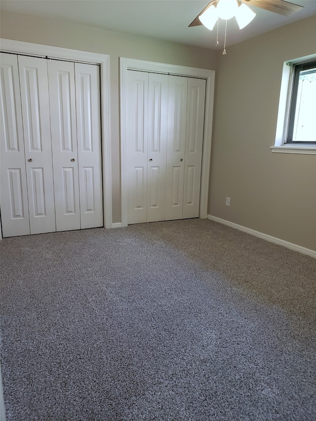 unfurnished bedroom featuring carpet flooring, ceiling fan, and two closets