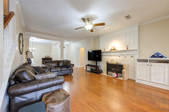 living room with a textured ceiling, ceiling fan with notable chandelier, a premium fireplace, light hardwood / wood-style flooring, and ornamental molding