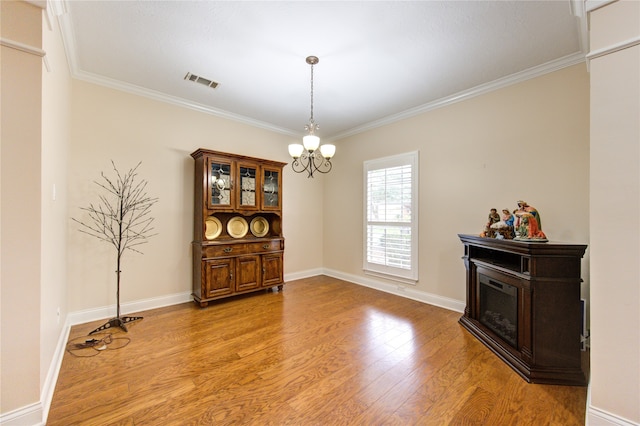 dining room featuring light wood-type flooring, crown molding, a fireplace, and a notable chandelier