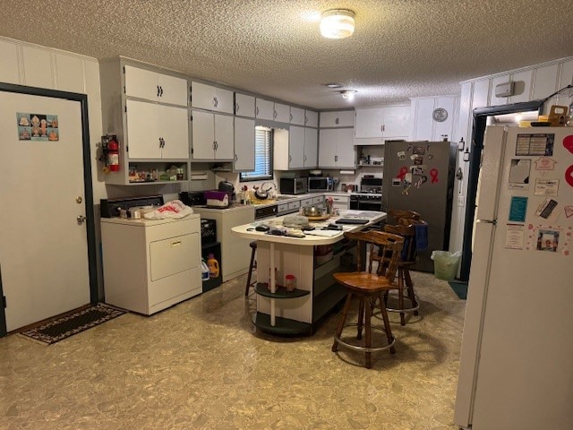 kitchen with a textured ceiling, appliances with stainless steel finishes, white cabinetry, and washer / dryer