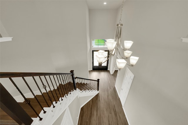 stairway featuring a towering ceiling, hardwood / wood-style floors, and a notable chandelier