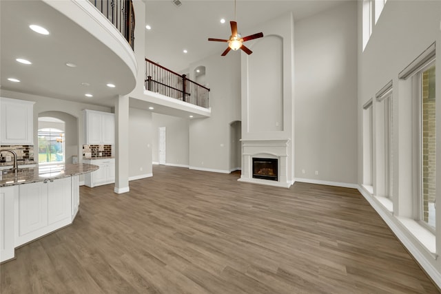 unfurnished living room with a towering ceiling, hardwood / wood-style flooring, sink, and ceiling fan