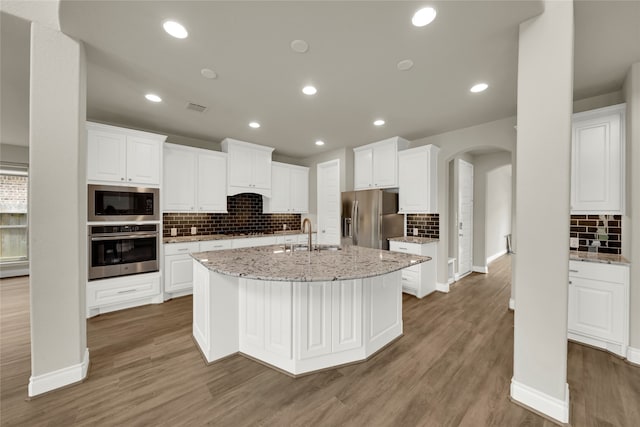 kitchen with dark wood-type flooring, white cabinets, appliances with stainless steel finishes, and an island with sink