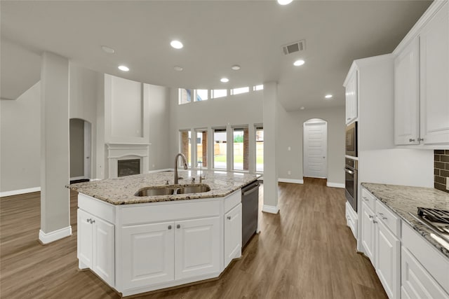 kitchen featuring a kitchen island with sink, light stone counters, sink, appliances with stainless steel finishes, and white cabinets