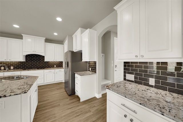 kitchen with stainless steel fridge, white cabinetry, and sink