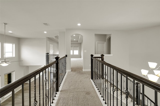 hall with light carpet, a wealth of natural light, and a notable chandelier