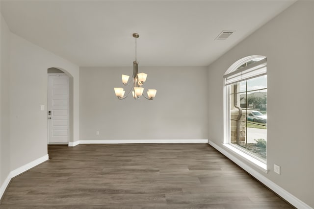 unfurnished room featuring dark wood-type flooring, plenty of natural light, and a notable chandelier