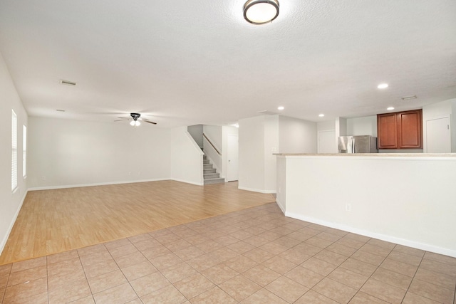 unfurnished living room with ceiling fan, a textured ceiling, and light hardwood / wood-style flooring