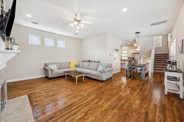 living room with ceiling fan, dark hardwood / wood-style flooring, a tiled fireplace, and a wealth of natural light