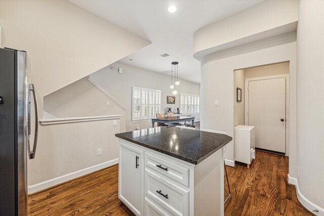 kitchen with decorative light fixtures, a center island, stainless steel fridge, dark stone counters, and white cabinets