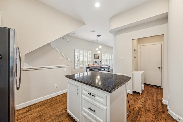 kitchen with white cabinetry, dark stone countertops, stainless steel fridge, a kitchen island, and pendant lighting